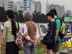 许多路过的游客，围观在法轮功的真相图片展前